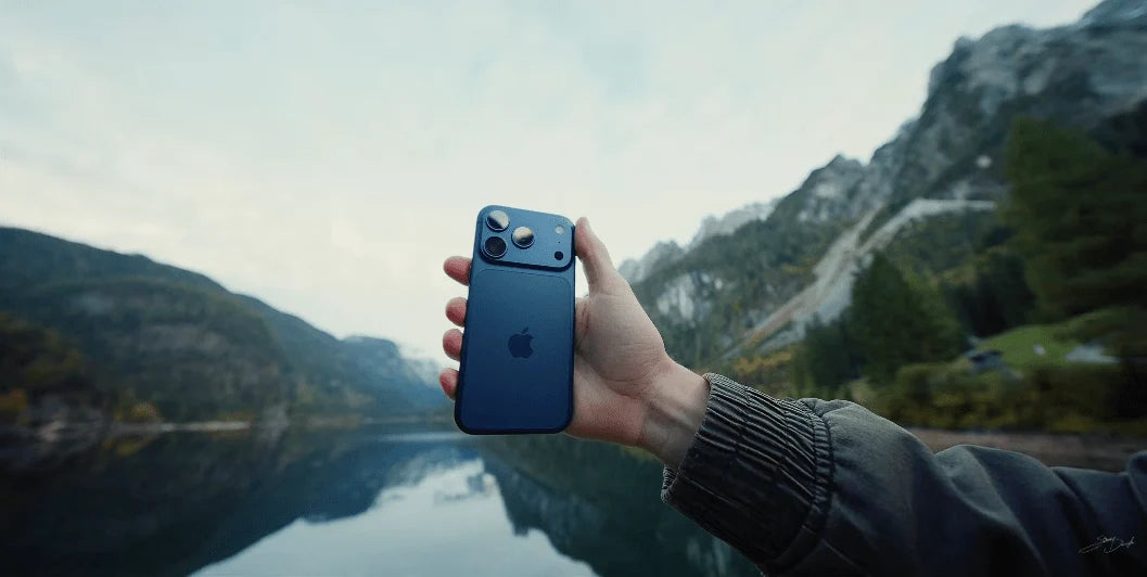 Hand hält ein dunkelblaues iPhone vor einer Berglandschaft am See